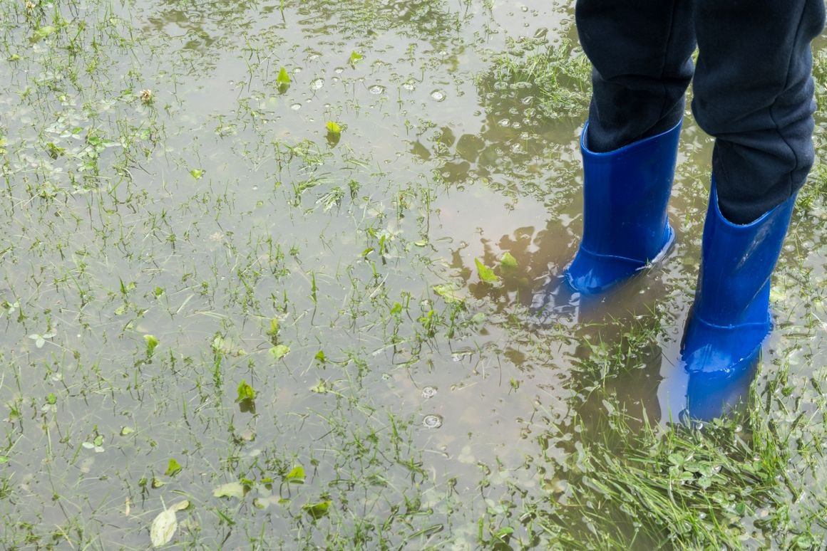 Person mit Gummistiefeln in überschwemmtem Garten
